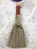   Brown Tigers Eye Tree of Life Broom - Grounding, Protection and Strength  This besom is a versatile handheld broom of stiff grass, bound with green cord and decorated with a silver Triquetra symbol charm with Tigers Eye crystals.